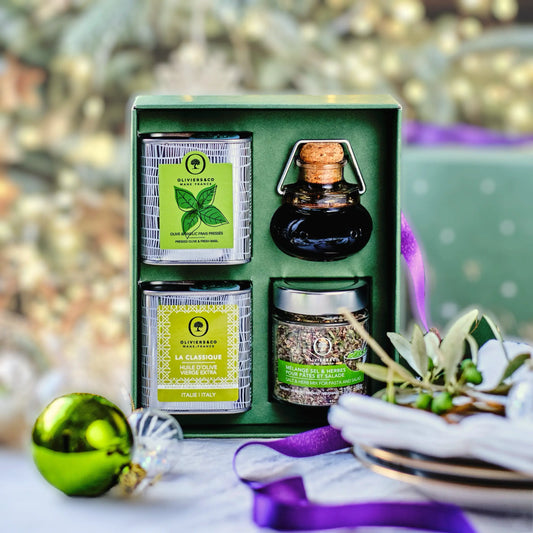 Hochwertige Olivenöl und Feinkost Geschenkbox mit festlicher Dekoration im Hintergrund. Enthalten sind frisches Basilikum-Olivenöl, klassisches extra natives Olivenöl und eine Flasche dunklen Balsamico-Essigs. Eine perfekte Auswahl für ein luxuriöses Gourmet-Geschenk zu Weihnachten oder für besondere Anlässe