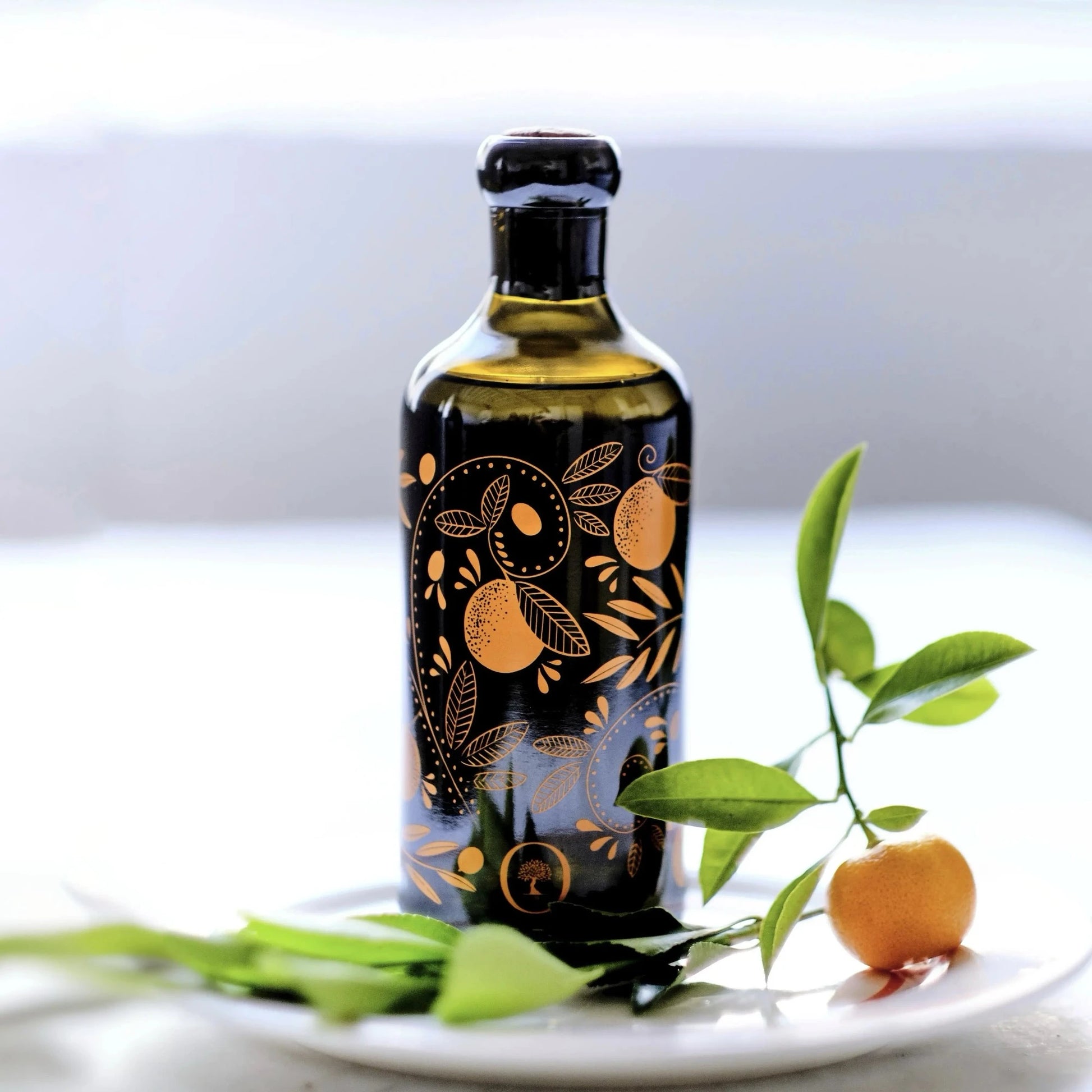  flasche mit olivenöl mit mandarinenaroma, verziert mit orangen mustern, auf einem teller mit einer frischen mandarine und grünen blättern im vordergrund