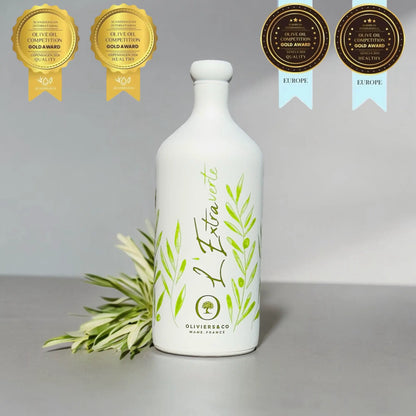 eine flasche testsieger olivenöl "l'extraverte" von oliviers & co, mane, france. umgeben von vier medaillen für qualität und gesundheit aus skandinavien und europa olivenöl test. im hintergrund olivenzweige